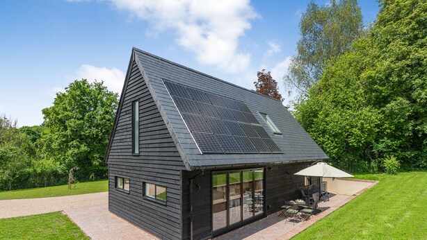Et moderne hus med et skråt tag, solpaneler og en terrasse med havemøbler.
