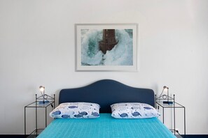 Un lit avec une couvre-lit bleue, deux oreillers assortis, une tête de lit et un tableau encadré représentant un phare, accroché au mur.