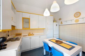 Une cuisine avec des meubles blancs, des touches de jaune, une cuisinière et une table à manger entourée de chaises bleues.