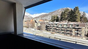 Udsigt fra et vindue med et bjerglandskab i baggrunden, med moderne bygninger og altaner.