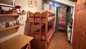 Et værelse med køjeseng i træ, skrivebord og reoler, en radiator og en dør til et andet rum.