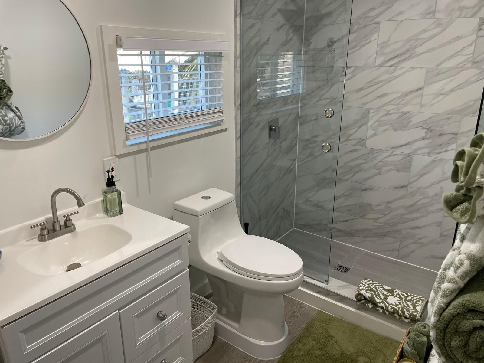 Ein Badezimmer mit weißem Waschbecken, Spiegel, Toilette und Dusche mit Marmorfliesen.