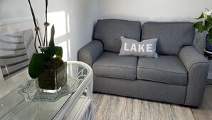 Ein Wohnzimmer mit grauem Sofa, einem Glastisch mit dekorativer Vase und einer Wanduhr.