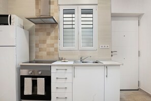 Una cocina compacta con horno integrado, microondas, extractor de acero inoxidable, pileta doble y ventana esmerilada.