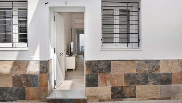 A hallway with a door leading to a room, a window with metal bars, and a tiled wall.