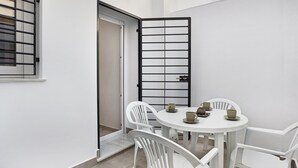 A white dining table with four chairs, a door with a black metal gate, and a window with a metal grille.
