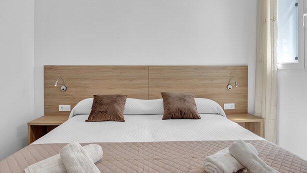 Una habitación de hotel moderna con cabecera de madera, dos almohadas, una cama con cubrecama acolchado y una mesita de noche.