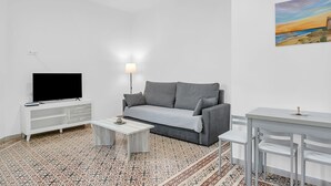 Una sala de estar moderna con un sofá gris, un mueble blanco para el televisor, una mesita de centro pequeña y un suelo estampado.