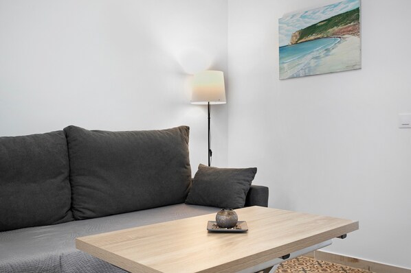 Una sala de estar moderna con un sofá, una mesita, una lámpara y un cuadro en la pared.