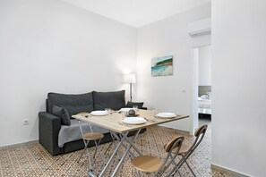A small, modern room with a dining table, chairs, a sofa, and a lamp.