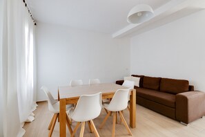 A modern dining area with a wooden table and white chairs, a brown sofa, and a white ceiling light.