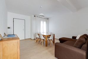 A modern living room with a brown sofa, a wooden dining table with white chairs, and a white ceiling light.