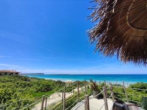 Un escalier en bois menant à une plage, avec un ciel bleu dégagé.