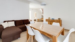 Ein modernes Wohnzimmer mit einem braunen Sofa, weißen Stühlen, einem Holzes Esstisch und einem Holzschrank.