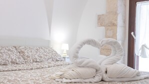 Una cama con una toalla dispuesta en forma de corazón, una lámpara y una pared de piedra.