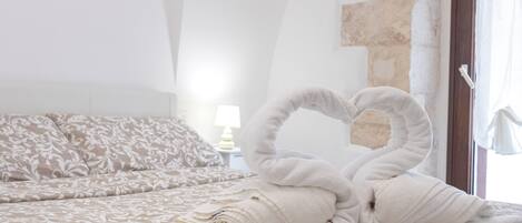 A bed with a heart-shaped towel arrangement, a lamp, and a stone wall.