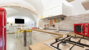Una cocina moderna con un refrigerador rojo, armarios blancos, una salpicadera de piedra y una estufa a gas.