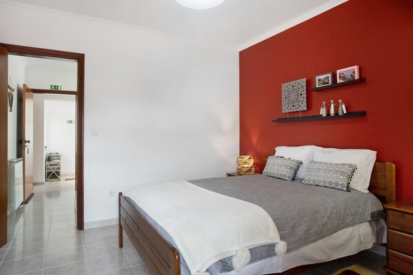 Une chambre à coucher avec un lit, un mur d’accent de couleur rouge et une porte donnant sur une autre pièce.