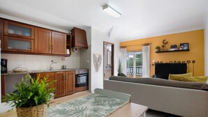 Un espacio habitable compacto con kitchenette, un sofá, una mesa de comedor con una planta y vistas al exterior.