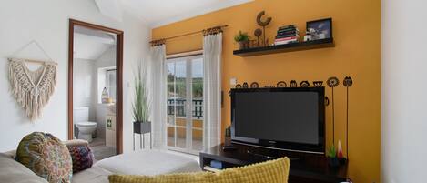 Una sala de estar con televisor, sofá y almohadones decorativos.