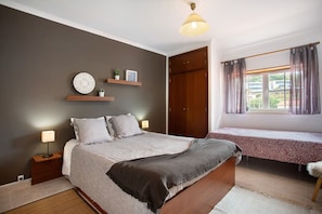 Une chambre à coucher comprenant un lit, une table de chevet, une lampe, une étagère avec des objets décoratifs, une armoire et une fenêtre avec des rideaux.