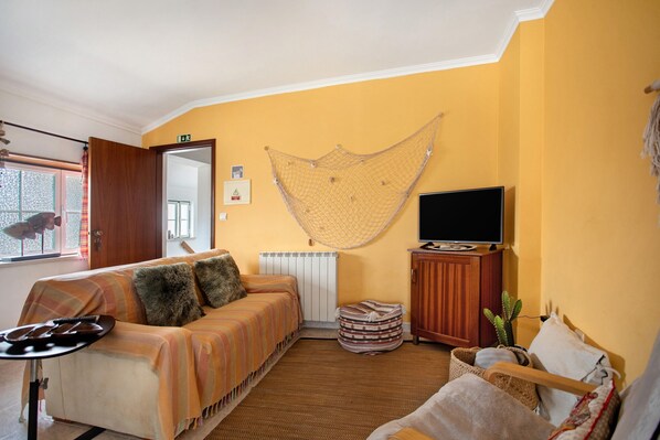Een woonkamer met een bank, een televisie, een hangmat en een cactus.