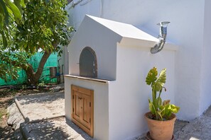 A small outdoor kitchen with a chimney, a wooden door, and a potted plant.