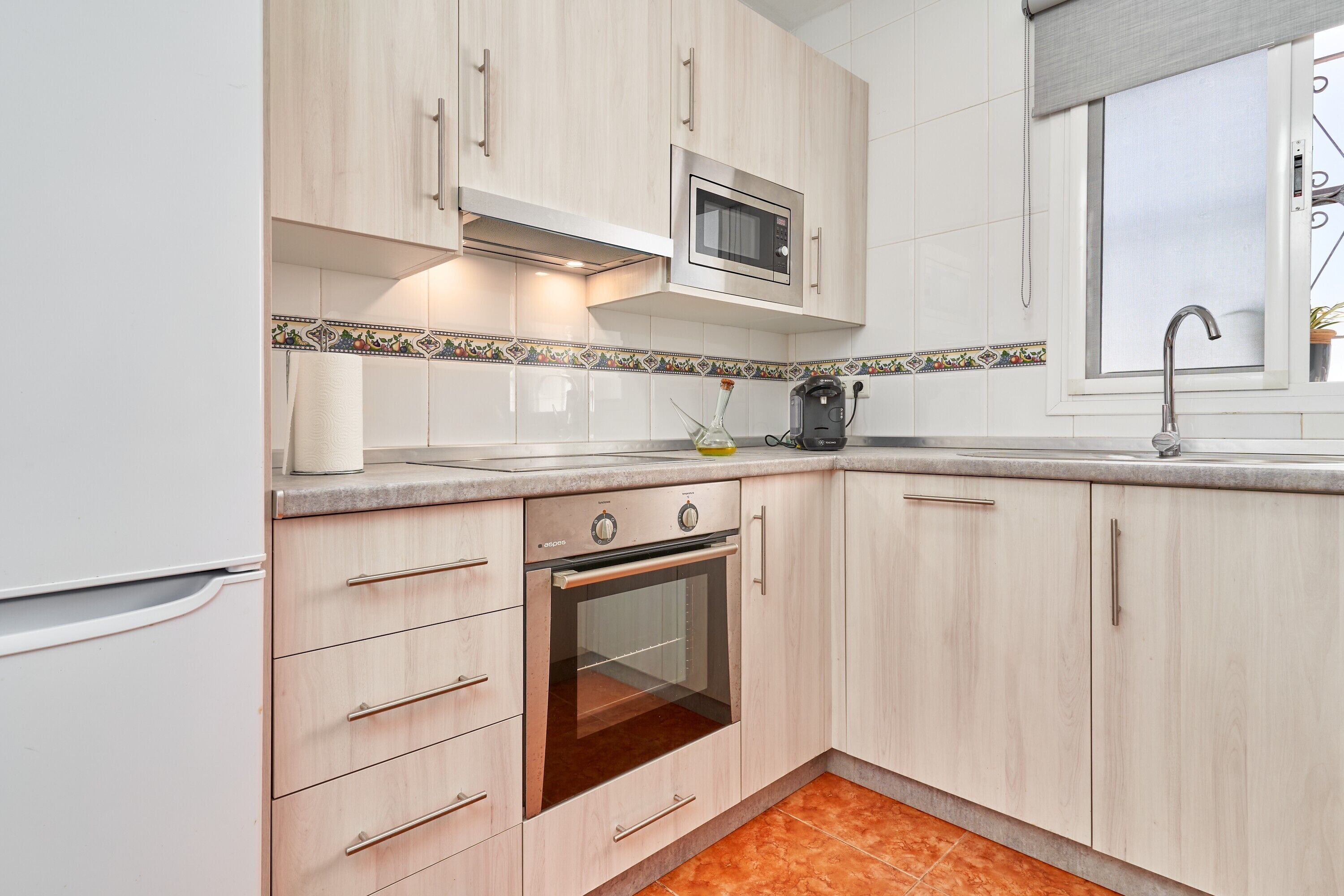 A kitchen with light wood cabinets, a built-in oven, a microwave, and a window with a view.