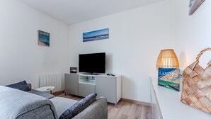 A modern living room with a sofa, a TV, a small table, and a lamp.