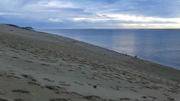 A beach with footprints leading to the water, a clear sky, and distant mountains.