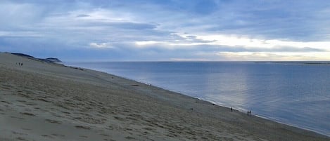 A beach with footprints leading to the water, a clear sky, and distant mountains.