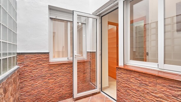 Une pièce d’angle avec une porte-fenêtre coulissante, une fenêtre et un mur en pierre.