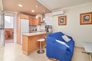 Une cuisine compacte dotée d’appareils électroménagers modernes, d’un tabouret de bar et d’un canapé bleu.