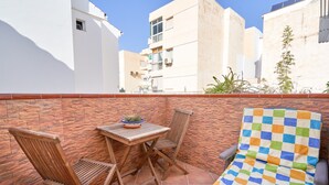 Une terrasse avec un coussin à carreaux, des chaises en bois et une petite table agrémentée d’une plante.