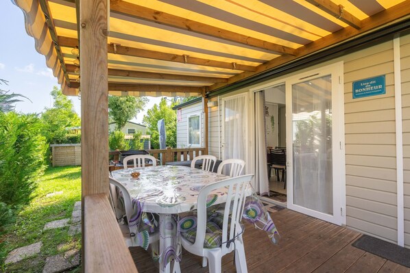 A covered patio with a table and chairs, a wooden deck, and a sliding glass door leading to a covered area.