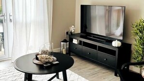 A living room with a flat-screen TV, a coffee table, and a plant.