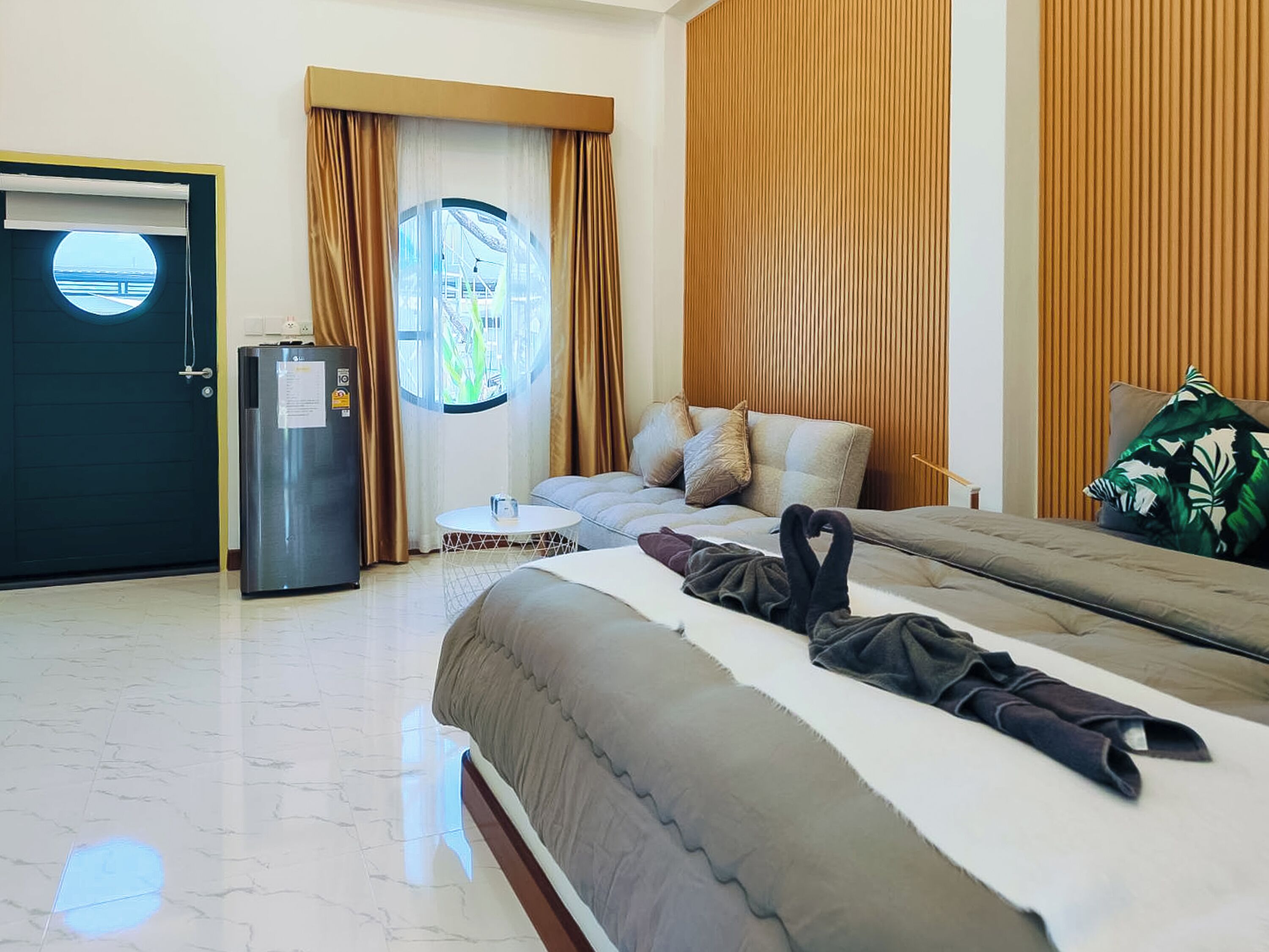 Habitación de hotel con cama, una mesita redonda, refrigerador y ventana con cortinas.