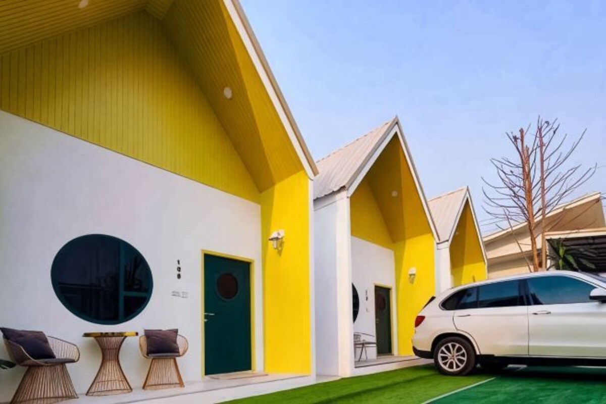 A modern building with a yellow facade, a green door, and a white car parked in front.