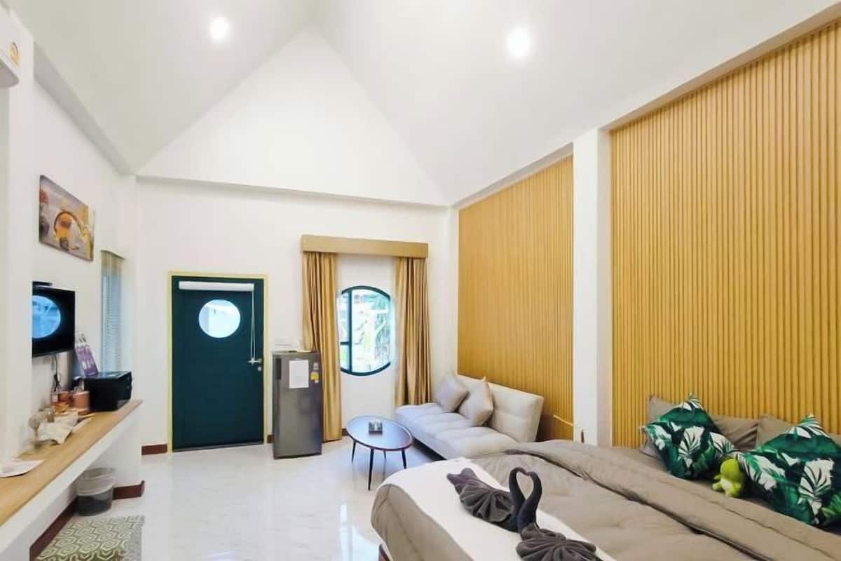Habitación de hotel con cama, sofá, escritorio con computadora, televisor y ventana con cortinas.
