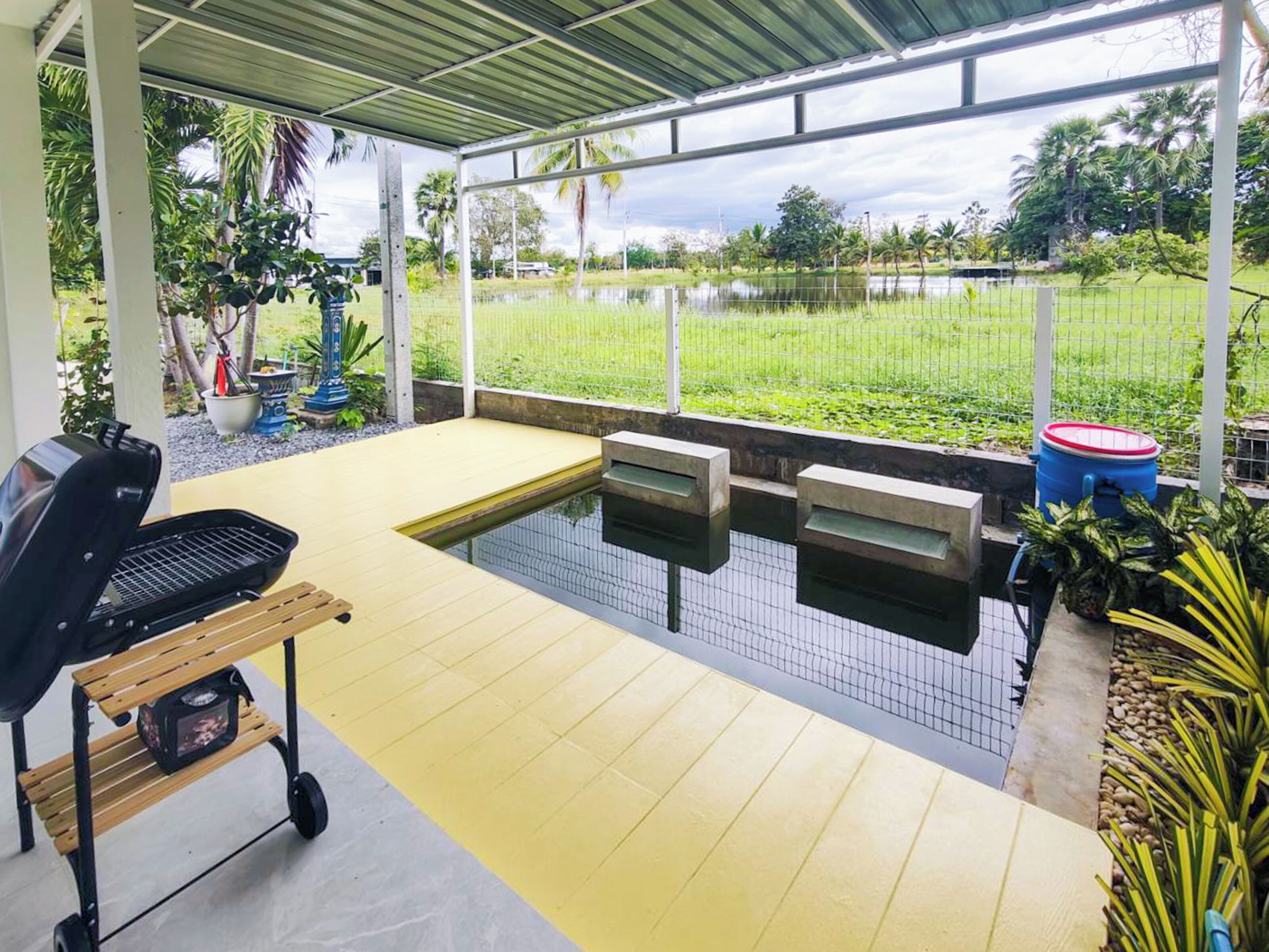 Un espacio al aire libre techado con piscina, parrilla y vista a un campo cubierto de césped.