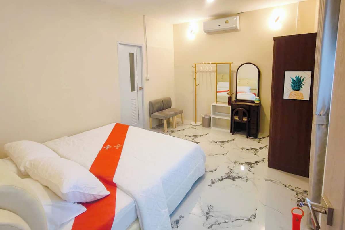 Una habitación de hotel con cama, una banca, un espejo, una mesita y una puerta.