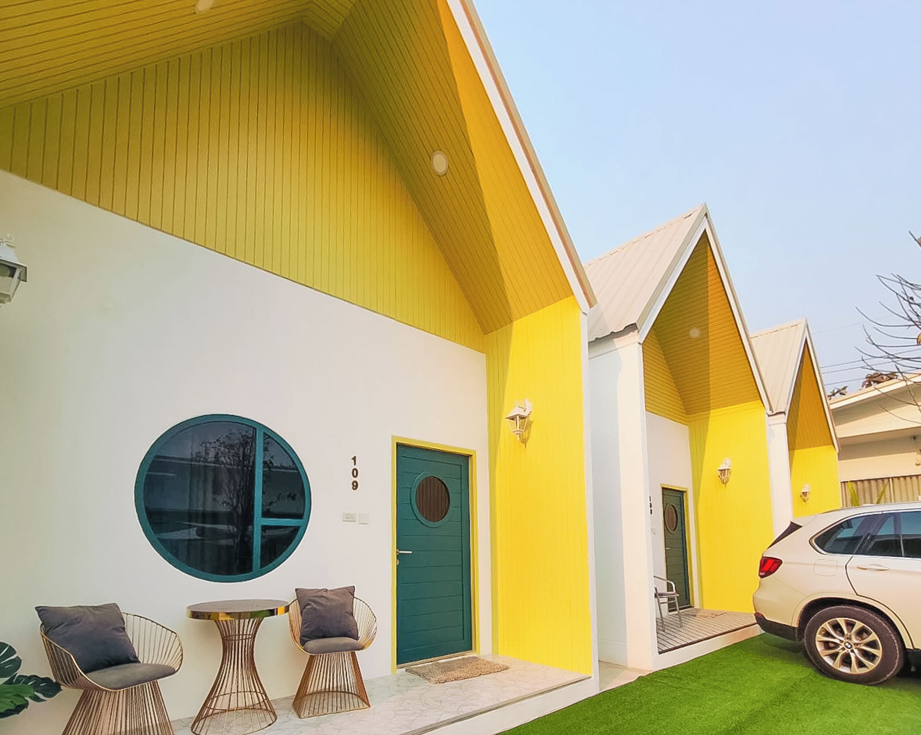 Un edificio amarillo con una puerta verde, un ventanal redondo y un coche estacionado adelante.