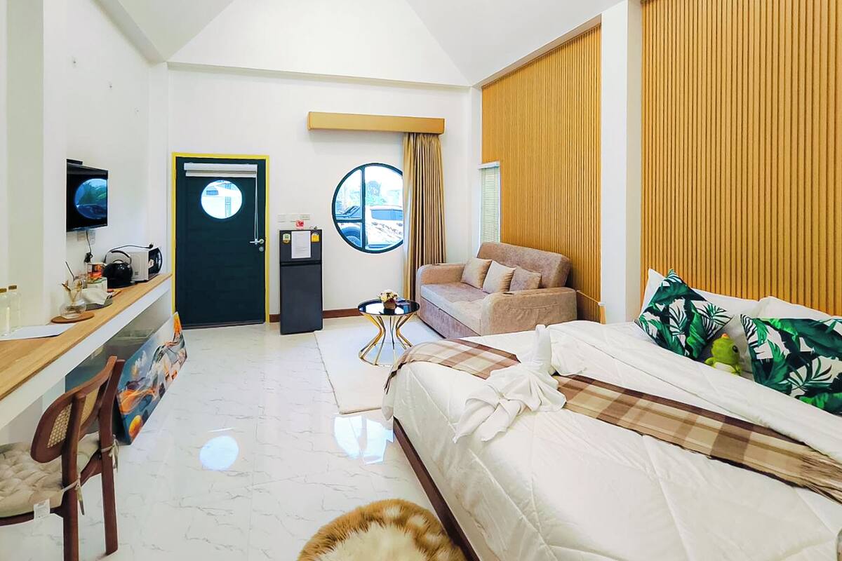 Una habitación de hotel con cama, sofá, escritorio con computadora, televisor y ventana con cortinas.
