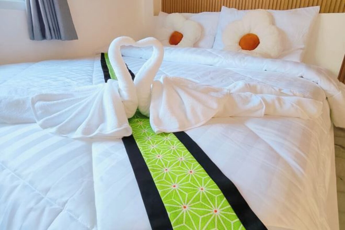 A hotel room with a neatly made bed, a green and black striped bedspread, and two swan-shaped pillows.