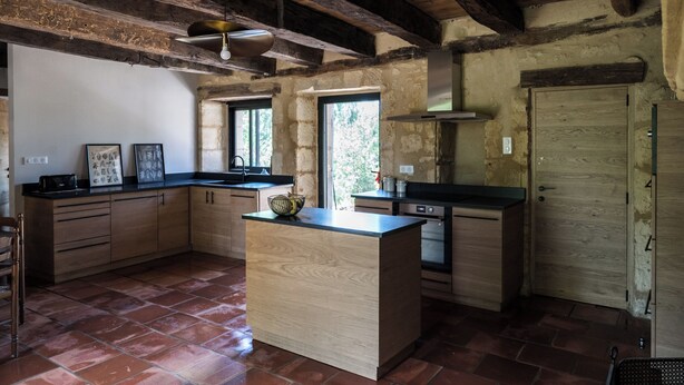 A rustic kitchen with exposed wooden beams, a central island, and a large window providing natural light. - Les Hauts de Couze, old stones, natural surroundings (Lalinde)