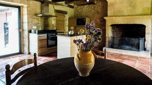 A rustic dining area with a wooden table, a vase with dried flowers, and a fireplace in the background. - Les Hauts de Couze, old stones, natural surroundings (Lalinde)