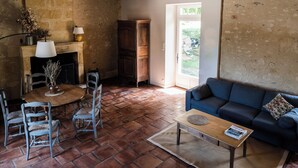 A rustic living room with a stone fireplace, wooden dining table, and blue sofa. - Les Hauts de Couze, old stones, natural surroundings (Lalinde)