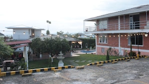 A building with a brick facade and a balcony, surrounded by a garden with a fountain and trees. - Hotel campestre sueño del abuelo (Pereira)