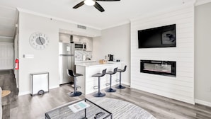 A modern kitchen with stainless steel appliances, a microwave, and a coffee maker. There is a bar area with stools and a large clock on the wall. - Battleship Sunset on Water Street! River View! Free parking!! (Wilmington)