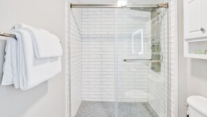A modern shower with a glass door, white tiled walls, and a tiled floor. - Battleship Sunset on Water Street! River View! Free parking!! (Wilmington)